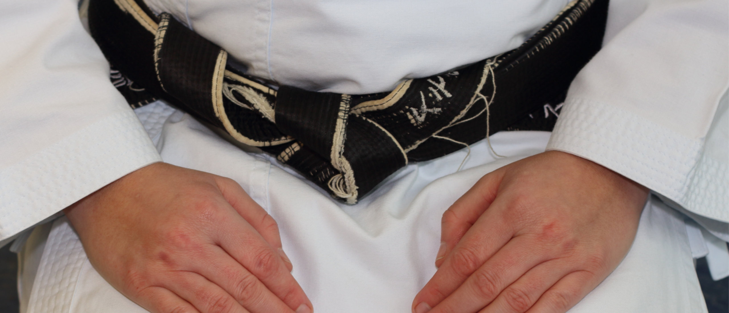 Nahaufnahme des schwarzen Gürtels und der Hände eines Karateka im Karate-Gi